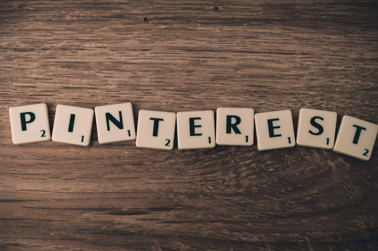 Scrabble tiles spelling Pinterest on a wooden background, symbolizing social media and creativity.