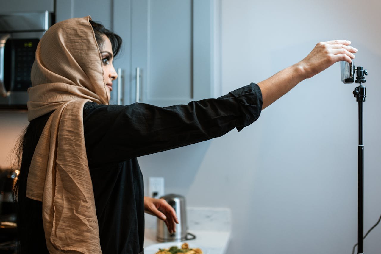 A Muslim woman in a hijab records a cooking video in her kitchen, focusing on her food presentation.