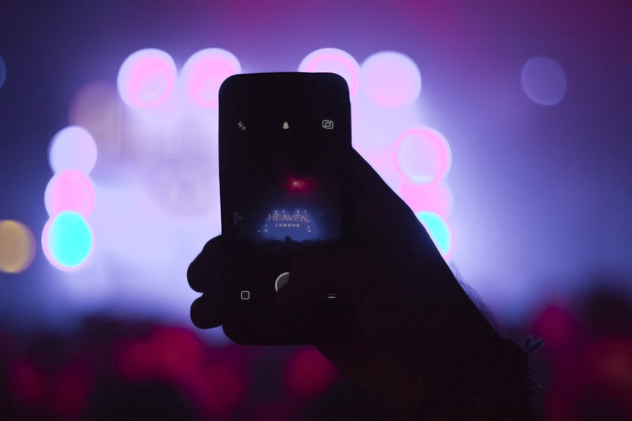 Silhouette of a smartphone capturing lively nightlife with colorful bokeh lights.